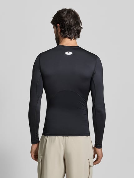 Męski model nosi Slim Fit Longsleeve mit Logo-Print von Under Armour, elastyczny materiał, krój slim fit, czarny, widok całej sylwetki od tyłu.