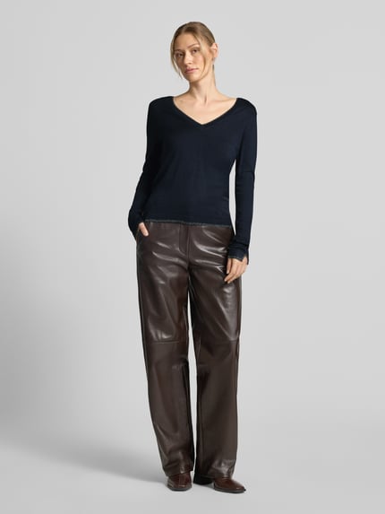 Frauenmodel trägt Slim Fit Longsleeve aus reine Viskose Modell 'Maglia Chiusa' von Liu Jo White in Schwarz, glatte Struktur, V-Ausschnitt, Logo-Detail, kombiniert mit brauner Hose, Damen Longsleeve, Ganzkörperansicht von vorne.