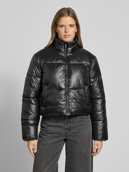 Frauenmodel trägt Puffer Jacket mit glänzender Optik von PIECES in Schwarz, cropped, Teilungsnähte, Reißverschluss, Ganzkörperansicht von vorne.