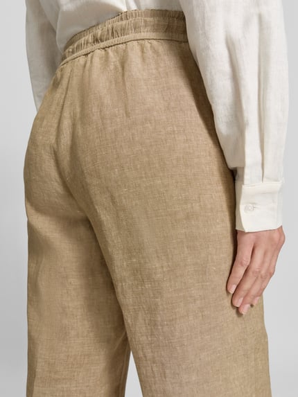 Frauenmodel trägt Regular Fit Weite Hose aus reinem Leinen Modell 'FARINA' von Brax, Optik: Unifarben, Textur leicht strukturiert, Label-Applikation, Bundabschluss elastisch mit Tunnelzug, Eingrifftasche, Material: reines Leinen, Nahaufnahme Rückansicht.
