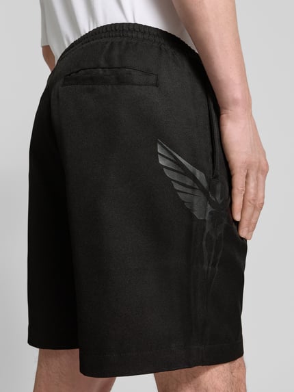 Männermodel trägt Shorts mit Logo und elastischem Bund von COLUCCI in Schwarz mit Eingrifftaschen, Regular-Fit, Ganzkörperansicht Rückansicht.