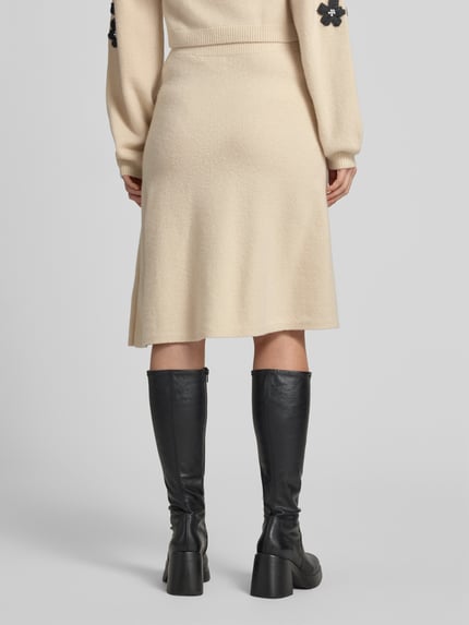 Frauenmodel trägt Knielanger Strickrock mit Stitchings und Perlen von Christian Berg Woman in Beige, reine Wolle, A-Linie, Ganzkörperansicht Rückansicht.