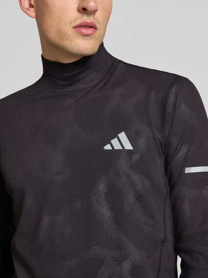 Męski model nosi Slim Fit Sport-Langarmshirt mit reflektierenden Details von adidas Training, czarno-szary wzór, zbliżenie na górną część ciała.