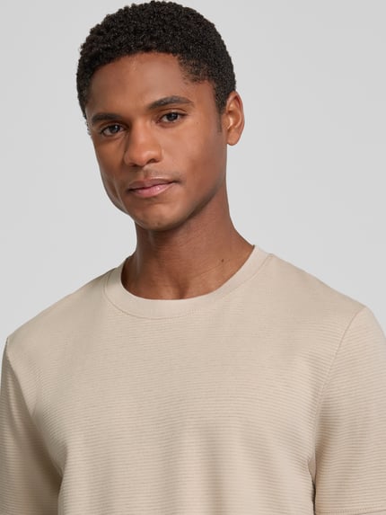 Męski model nosi Regular Fit T-Shirt aus Baumwoll-Mix von s.Oliver RED LABEL, jasny beż, gładka faktura, zbliżenie górnej części ciała.