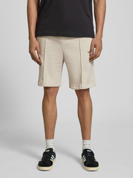 Männermodel trägt Sweatshorts mit Logo Modell 'KANE' von Jack & Jones aus Baumwoll-Mix, Relaxed-Fit, elastischer Bund, helle Farbe, Ganzkörperansicht von vorne. Bundweite 42 cm, Innenbeinlänge 19 cm bei Größe M.