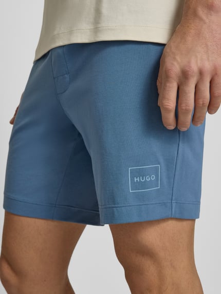 Męski model nosi Regular Fit Szorty z mieszanki bawełny Model 'LAZE' od HUGO, efekt: jednolity kolor, nadruk z logo, wyhaftowane logo, tunel, elastyczny ściągacz, boczne wpuszczane kieszenie, kolor jasnoniebieski, krótka faktura, widoczne szwy, mieszanka bawełny, detaliczna perspektywa, zbliżenie na uda.