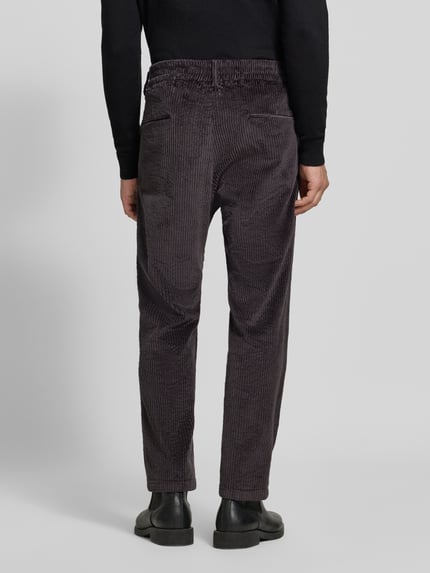 Männermodel trägt Straight Fit Hose aus Baumwoll-Mix Modell 'Chasy' von DRYKORN in Cord-Optik, dunkle Farbe, Gesäßtaschen, Ganzkörperansicht Rückansicht.