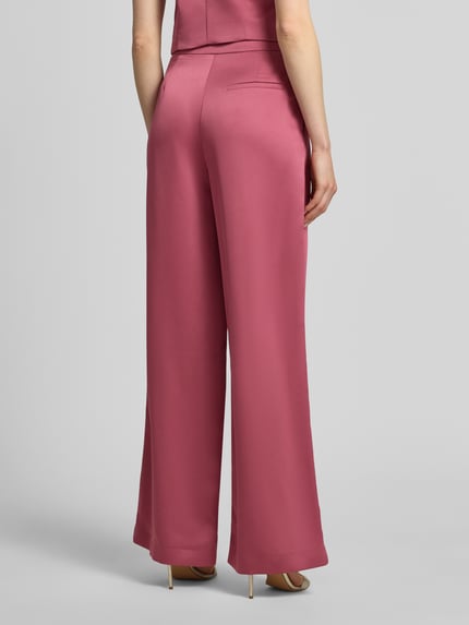 Frauenmodel trägt Hose mit weitem Bein und Falten von Jake*s Cocktail aus Satin in Rosa mit Gesäßtasche, Ganzkörperansicht Rückansicht. Bundweite 34 cm, Innenbeinlänge 82 cm in Größe 36.