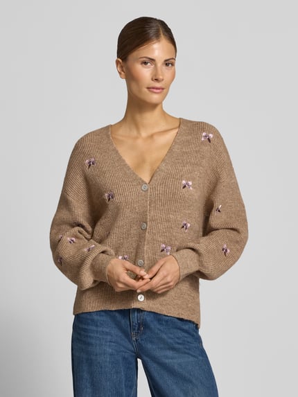 Frauenmodel trägt Relaxed Fit Strickjacke aus elastischem Woll-Mix Modell 'FLEUR' von YAS, beige mit floraler Stickerei, V-Ausschnitt, Knopfleiste, Ganzkörperansicht von vorne