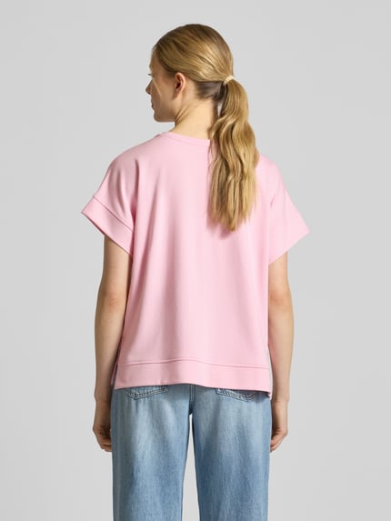 Modelka nosi T-Shirt aus Viskose-Mix mit Pailletten od Milano Italy, różowy, krój regular fit, okrągły dekolt, długość tyłu w rozmiarze S: 56 cm, widok całej sylwetki od tyłu.