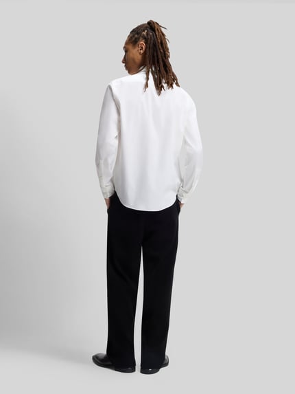 Męski model nosi Slim Fit Freizeithemd aus Baumwoll-Mix Modell 'ERMO' od HUGO, biała gładka tkanina, długie rękawy, widok całej sylwetki z tyłu.