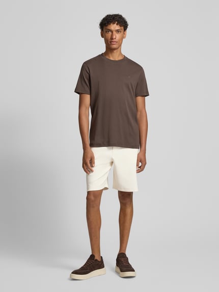 Mannenmodel draagt Shorts met steekzakken model 'Joseignacio' van JOOP! collectie in katoenmix met stretch, loose fit, elastische band met tunnelkoord, labelpatch, kleur lichtbeige; geheel vooraanzicht.