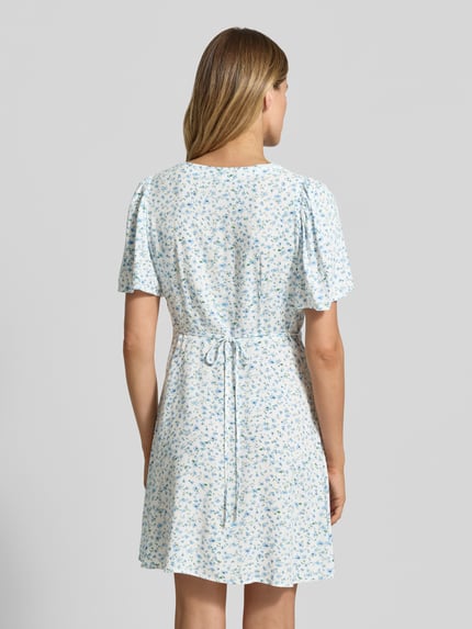 Vrouwenmodel draagt Leicht ausgestelltes Minikleid aus reiner Viskose Modell 'ALBA' van Vero Moda, look: effen kleuren, licht uitlopend, minilengte, V-hals, tailleriem, knoopsluiting, korte mouw, wijde mouwen, materiaal: zuiver viscose. Ganzkörperaanzicht achteraan.