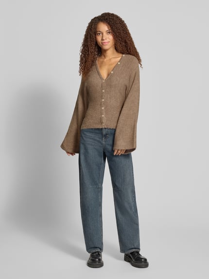 Vrouwenmodel draagt Regular Fit gebreid jack met wol van Gina Tricot, elastische materiaalmix, ribboorden, knoopsluiting, met lange mouwen, ruglengte maat S 53 cm, mouwlengte maat S 49 cm, effen bruin, grof gebreide textuur, regular fit, voorkant volledig zichtbaar, Ganzkörperansicht von vorne.
