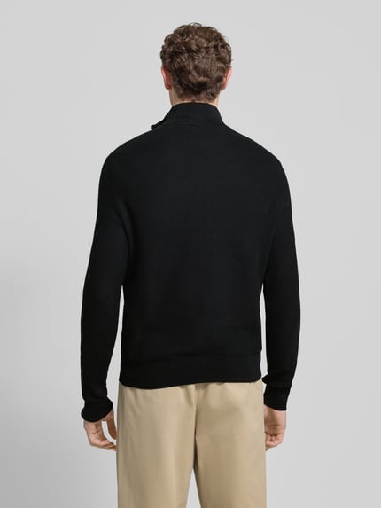 Męski model nosi Sweter z dzianiny z wyhaftowanym logo od Polo Ralph Lauren, bawełna, krój regular fit, prążkowane wykończenia, stójka, długość tyłu 70 cm, długość rękawa 68 cm, widok całej sylwetki z tyłu.