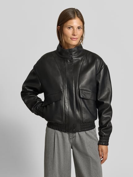 Frauenmodel trägt Lederjacke aus echtem Leder von MYON in Schwarz, lockere Passform, Stehkragen, Pattentaschen, Nahaufnahme Oberkörper.