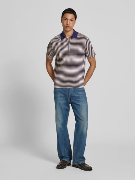 Męski model nosi Slim Fit Poloshirt in Strick-Optik od Closed z bawełny, krój slim fit, krótkie rękawy, kołnierzyk polo z zamkiem błyskawicznym, imitacja dzianiny, długość tyłu w rozmiarze M: 69 cm, widok całej sylwetki z przodu.