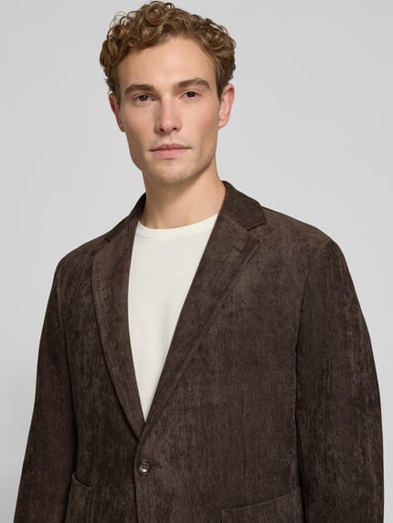 Männermodel trägt Regular Fit Sakko mit Reverskragen Modell 'BENITO' von CINQUE, braune Textur, elastischer Material-Mix, Nahaufnahme Oberkörper. Kontext: Herren Sakko, aufgesetzte Taschen, Rückenlänge 74 cm, Schulterbreite 42 cm, Ärmellänge 65 cm.