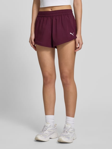 Frauenmodel trägt Regular Fit Sportshorts mit Logo-Print von PUMA in Dunkelrot, elastischer Bund, glatte Textur, Ganzkörperansicht von vorne, Damen Sportshorts von PUMA Performance.
